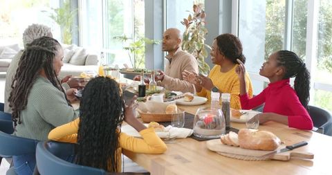 Multigenerational Black family sharing homemade meal around sunlit wooden table