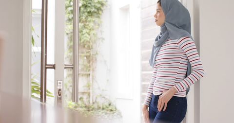 Thoughtful Female in Hijab Standing by Window at Home