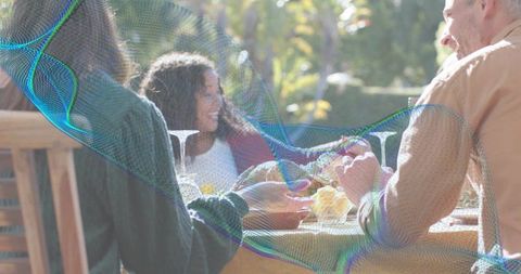 Sharing Bread During Sunlit Backyard Meal, Friends Reaching Across Table for Casual Outdoor Dining