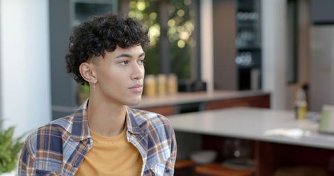 Young asian man wearing plaid shirt and cross earring sitting at modern kitchen counter