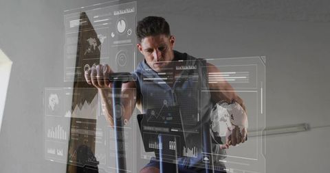 Fit man pedaling on stationary bike holding medicine ball with holographic metrics