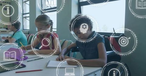 Elementary students studying with digital learning icons, focused girl writing at desk