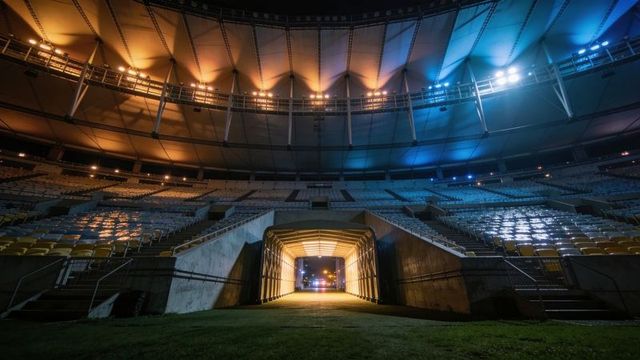 Illuminating stadium tunnel leading to field under dramatic blue and amber canopy lights