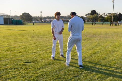 Two Cricket Teammates Coaching on Grass Field During Outdoor Training and Practice Drill