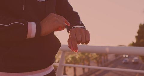 Person Utilizing Smartwatch on Urban Bridge at Sunset