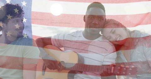 Friends playing guitar on beach with american flag overlay expressing patriotic unity
