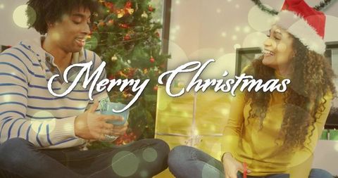 Couple Exchanging Christmas Gifts Beside Decorated Tree with Warm Bokeh Lights