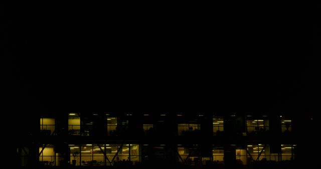 This image shows a nighttime view of an office building with lights on in various windows. It can be used in articles or presentations about late-night work culture, corporate life, or urban settings. It might also serve as a background for themes related to business and productivity.