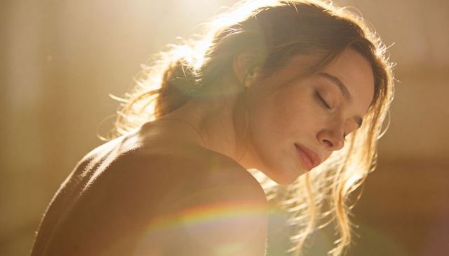 Young woman resting with closed eyes in golden backlight, soft glow and rainbow lens flare