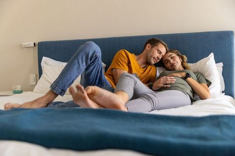 Expecting couple relaxing together on bed with blue headboard