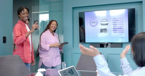 African American man presenting with smartphone while colleague uses tablet in modern meeting room