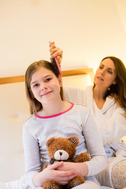 Mother combing her daughters hair in bedroom at home