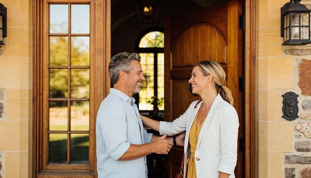 Couple greeting at arched front door, smiling reunion on sunny suburban home entrance