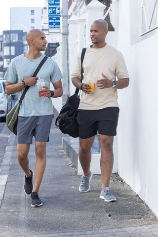 African american men walking together in casual sportswear carrying gym bags and drinks