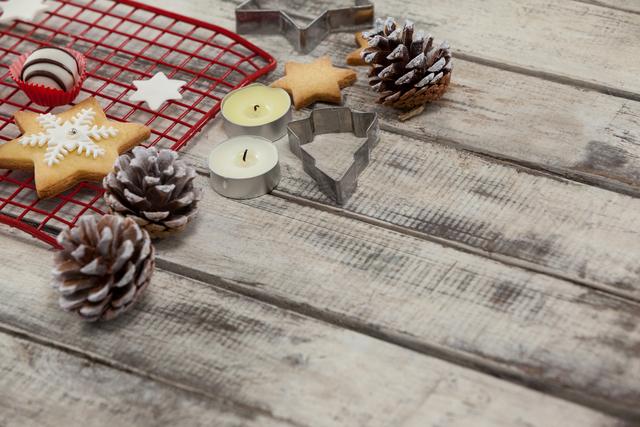 Christmas baking scene featuring cookie cutters, pine cones, and tealight candles on rustic wooden background. Ideal for holiday-themed advertisements, festive greeting cards, and seasonal blog posts. Perfect for promoting baking products, holiday decorations, and DIY craft ideas.