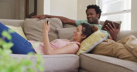 Happy Couple Relaxing on Sofa with Devices at Home