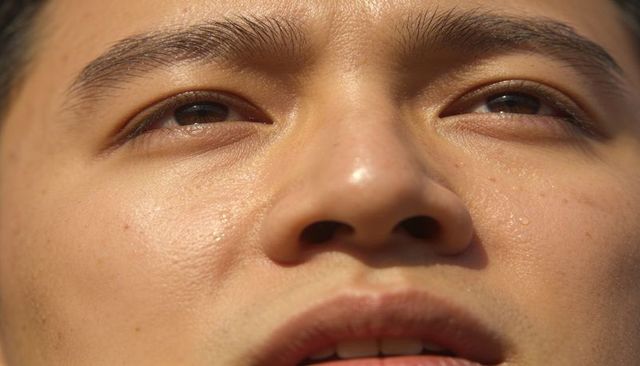 Asian woman squinting toward sun showing closeup skin texture, pores and sweat droplets