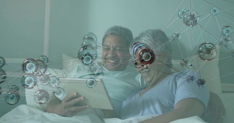 Senior couple smiling in bed using tablet with futuristic molecular network overlay for telehealth