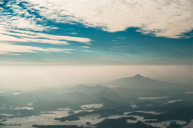 This image showcases a serene aerial view of a mountain range with foggy valleys stretching into the misty horizon. The cloudy sky enhances the peaceful atmosphere, creating a picturesque and tranquil scene. Perfect for use in travel brochures, nature documentaries, meditation apps, or as desktop wallpapers to inspire calmness and appreciation of natural beauty.
