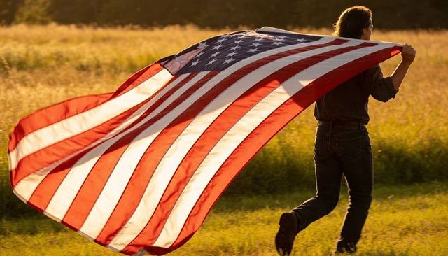 Man running with giant american flag through golden field at sunset for patriotic freedom