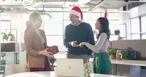 Diverse office team exchanging holiday gift laughing in sunlit modern workplace celebration