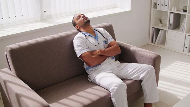 Male nurse resting on breakroom couch with stethoscope, daylight and minimal interior