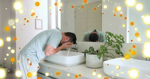 Washing face at modern bathroom sink, mature asian man leaning over white vessel basin