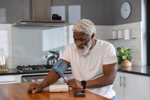 Senior man measuring blood pressure at sunlit kitchen island with home cuff monitor