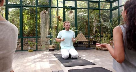 Group yoga meditation in sunlit glass house for wellness and flexibility