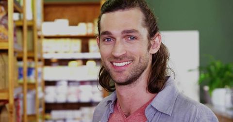 Smiling man standing in organic market with wooden shelves wearing casual shirt
