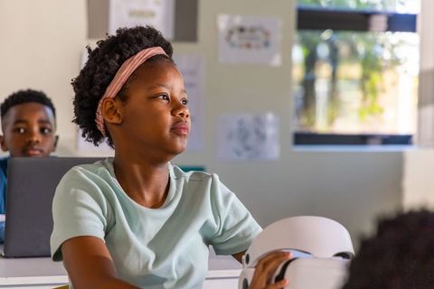 Preteen african american girl holding vr headset in classroom showing curiosity and focus