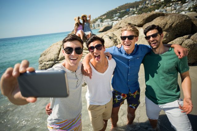 Cheerful male friends taking selfie at beach on sunny day