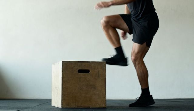 Male athlete performing knee drive next to wooden plyo box on rubber gym floor