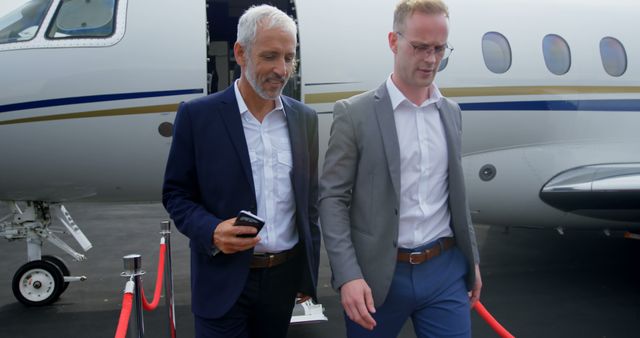 Businessmen walking away from a private jet, with copy space. The image captures a moment of corporate travel at an airport.