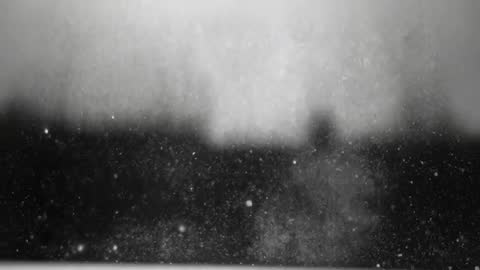 Slow-motion dust particles drifting across window forming central plume over dark horizon