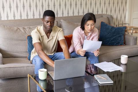 Young interracial couple reviewing finances on laptop and papers in cozy living room