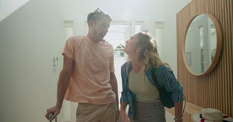 Cheerful couple arriving at vacation home with luggage in sunlight
