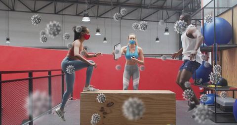Masked fitness team performing plyometric box jumps in industrial gym while coach timing