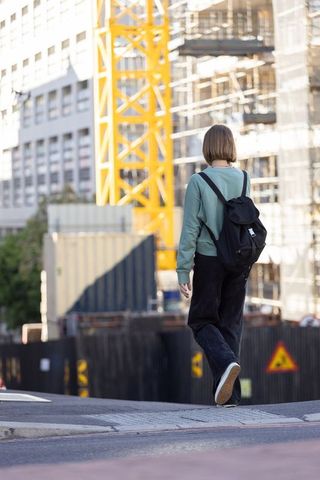 Young woman walking past urban construction site with backpack and yellow crane tower