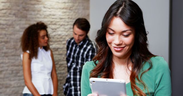 Smiling Woman Using Tablet While Colleagues Discussing in Background - Download Free Stock Images Pikwizard.com