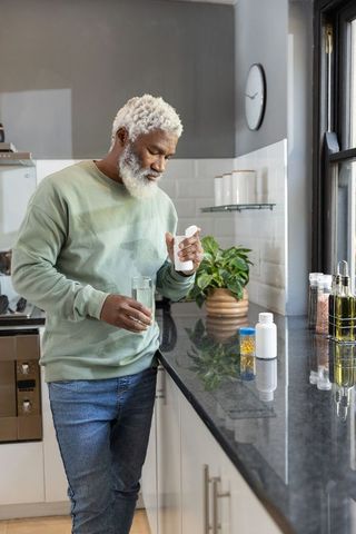 Senior african american man taking medication while holding glass of water in kitchen
