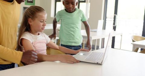 Diverse elementary students sharing laptop in modern classroom learning technology