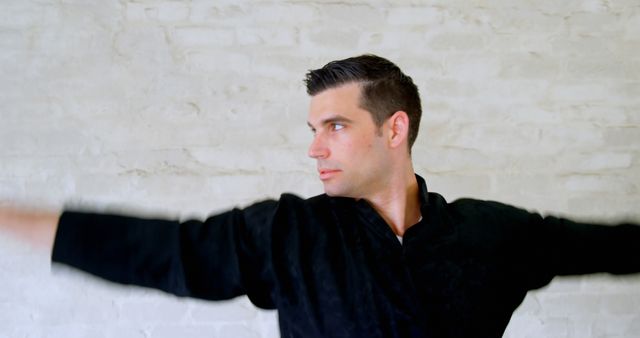 Caucasian man poses in a black shirt against a white wall. His confident stance suggests a professional or artistic setting, evoking a sense of purpose.