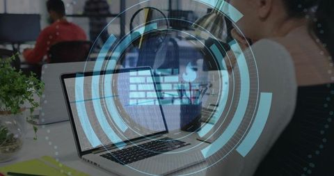 Woman Working on Laptop with Virtual Firewall HUD Overlay in Open-Plan Coworking Office