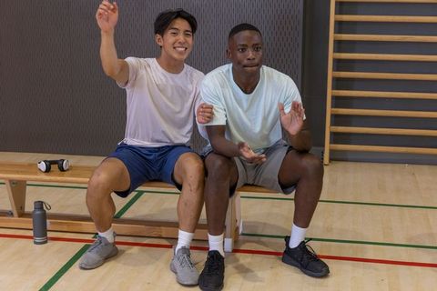 Two young men cheering and clapping on bench after indoor workout session