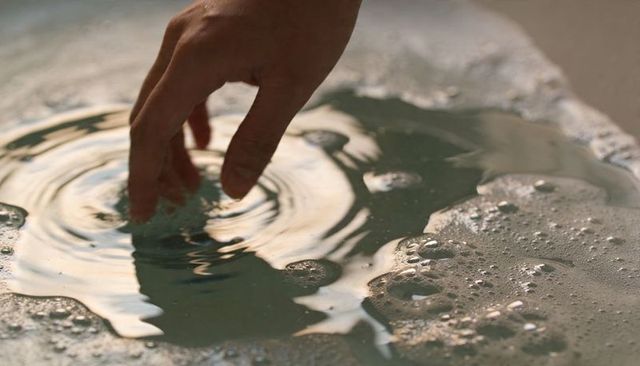 Hand touching bath water creating soft ripples and soap bubbles in warm reflective light