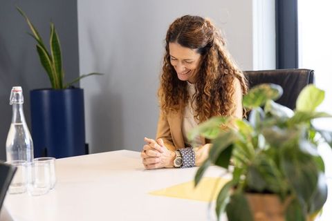 Smiling businesswoman sitting at conference table in sunlit modern office with plants