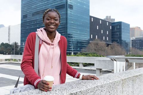 African american woman smiling on urban terrace holding coffee during morning commute