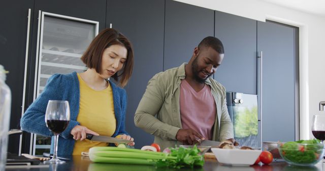 Image of happy diverse couple preparing food and smiling at each other in kitchen at home. Domestic life, love, health, happiness and inclusivity concept.