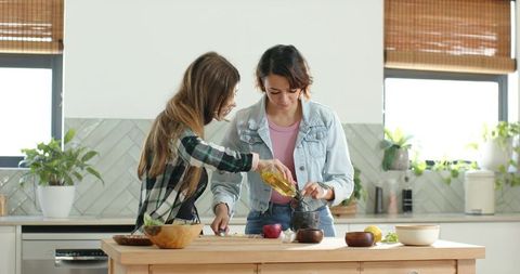 Friends cooking together pouring oil into mortar and chopping garlic on wooden kitchen island